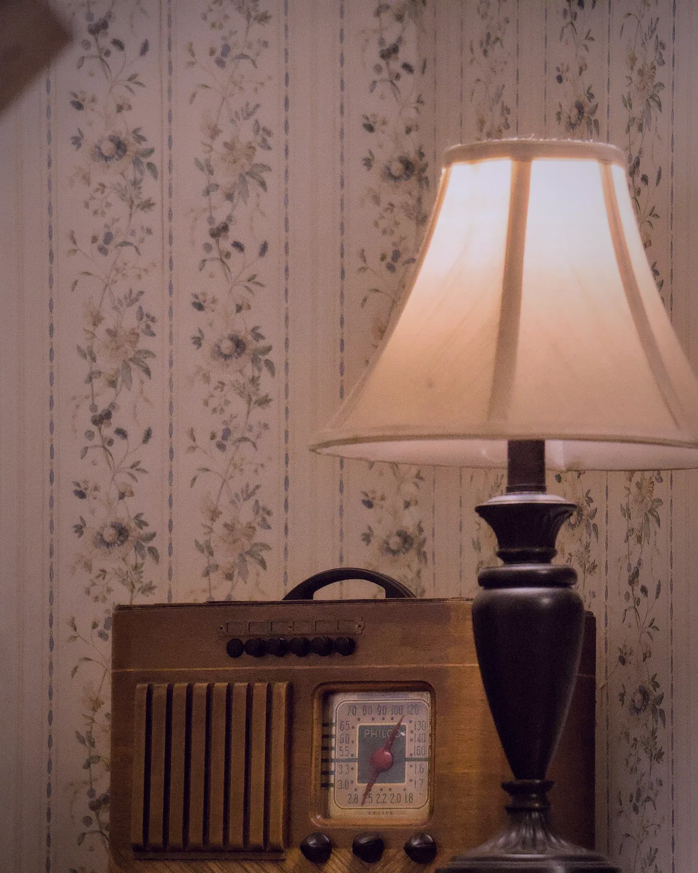 A lamp glowing against the room’s floral wallpaper before the doors open