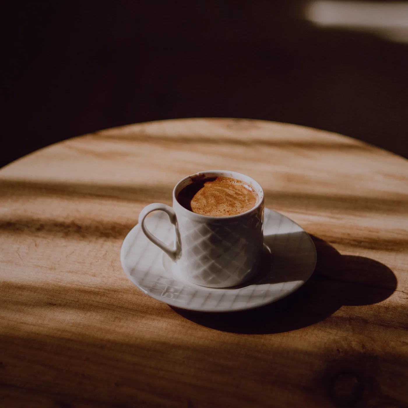A cup of coffee catching the light on the round wooden table